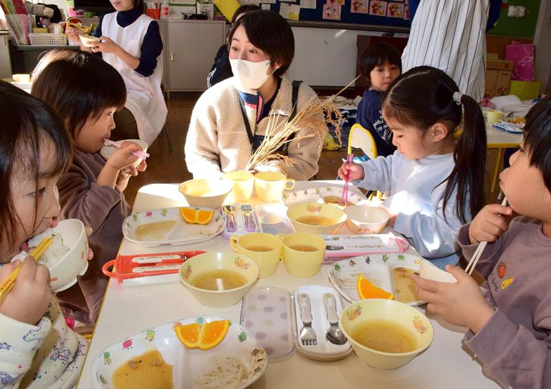 寄付した新米を頬張る園児に目を細める吉田さん（中央）＝８日、長南町立長南保育所