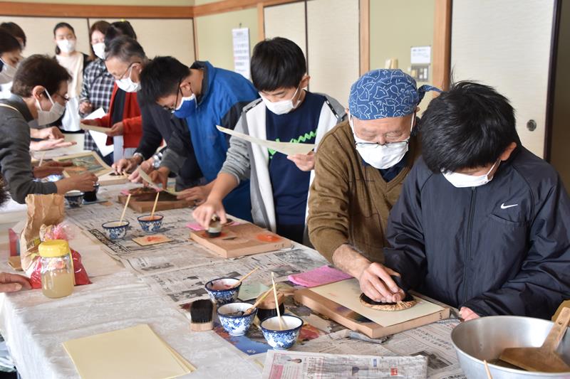 江戸木版画摺師（すりし）の松崎さん（右から２人目）から多色刷りのこつを教わる児童＝鋸南町立中央公民館