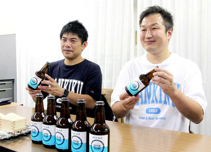 「ワールドビールアワーズ2022」ライスビール部門最高賞に輝いた「クジュウクリオーシャン・ライスエール」を見せる佐瀬代表(写真左)と風間さん=千葉市中央区