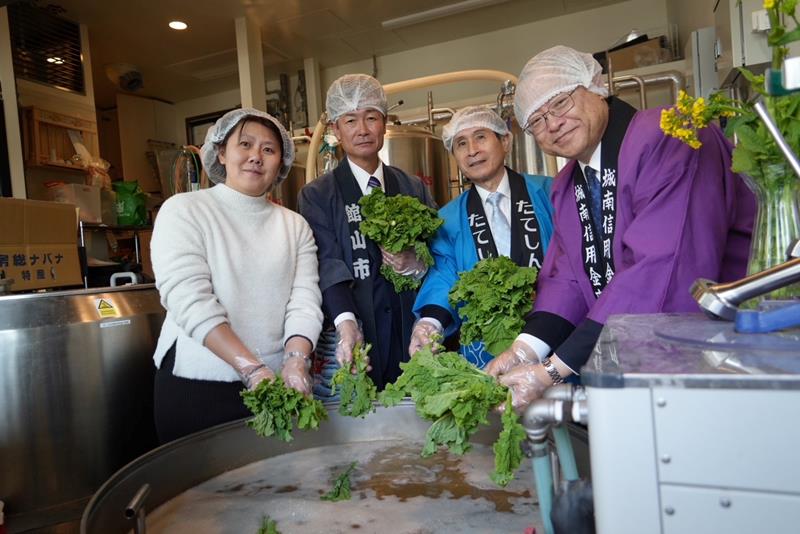 菜の花を醸造機に入れる川本理事長(右)ら=東京都