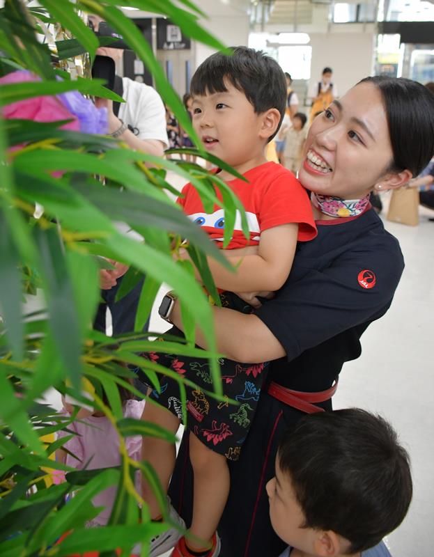 地上係員に抱きかかえられながら模造ササの高い位置に飾り付けする園児＝４日、成田市の成田空港