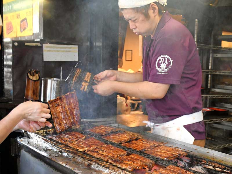 秘伝のタレを絡めた大きなうなぎのかば焼きを仕上げていく川豊の職人＝２４日、成田市