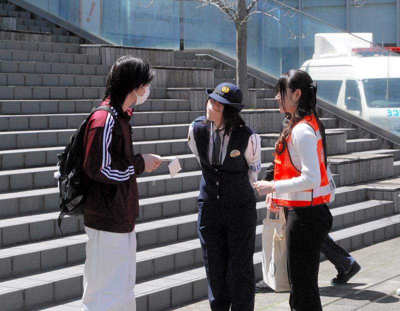 学生にチラシを配る警察官とボランティアの学生＝１６日午後０時２０分ごろ、松戸市