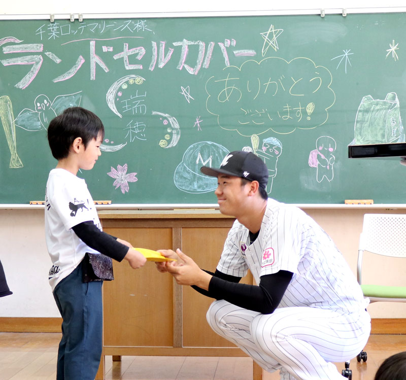 木村投手（右）からランドセルカバーを受け取る新１年生