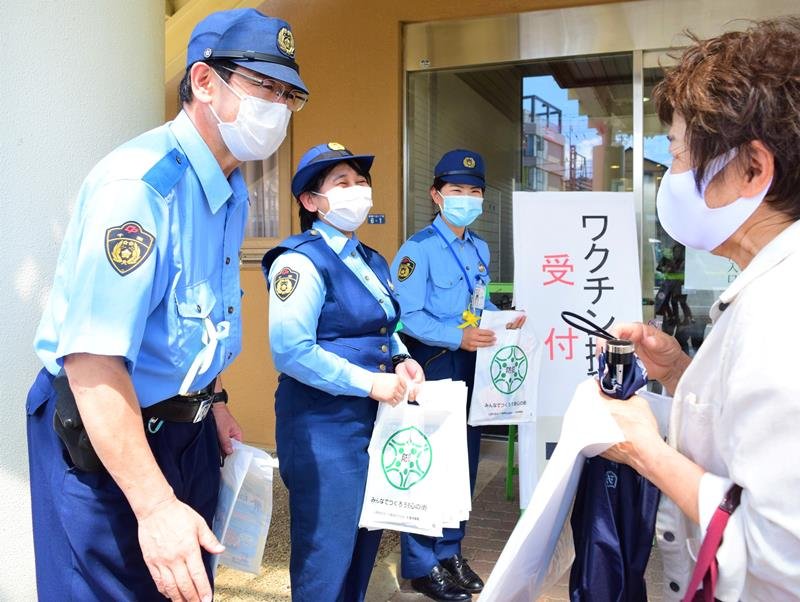 シトラスリボンを着け、新型コロナワクチン接種会場前で市民に詐欺への注意喚起を行う鎌ケ谷署員＝鎌ケ谷市
