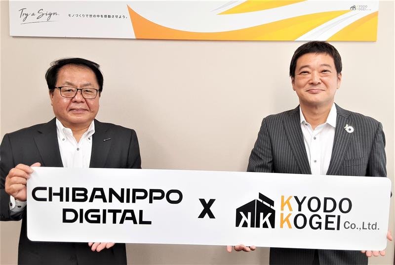 ビジネスマッチング契約を記念し、協同工芸社が制作した特製看板を手にする大澤社長（左）と箕輪社長
