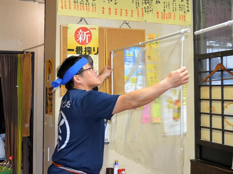 テーブル席に飛まつ対策のパーテーションを設置する店長の渡辺さん。「もう少しで外せると思っていたのに」と落胆した＝１７日午後４時半ごろ、千葉市中央区
