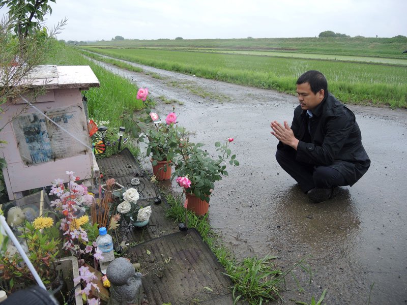 降りしきる雨の中、リンさんのほこらに手を合わせるハオさん＝１６日午前、我孫子市北新田

