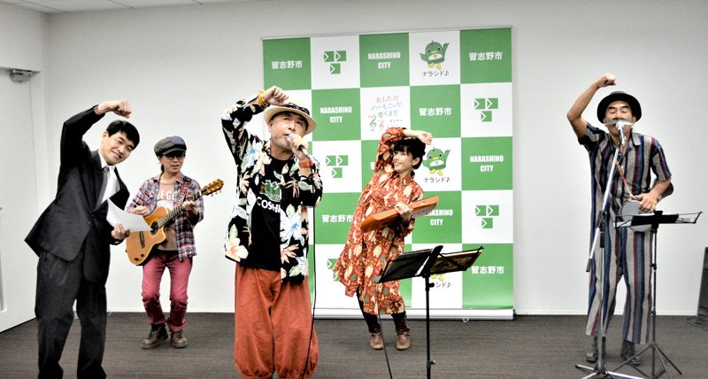 バンドメンバーと習志野の新たなご当地ソングを披露する田所さん（中央）。前列左は高校の同級生で作詞を担当した和菓子店主の堀さん＝習志野市役所
