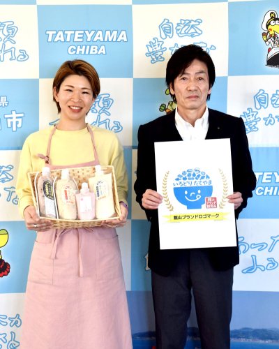 「館山ブランド」の認定を受けた甘酒を掲げる吉田さん（左）と、館山ブランドロゴマークを考案した阿部さん＝館山市役所