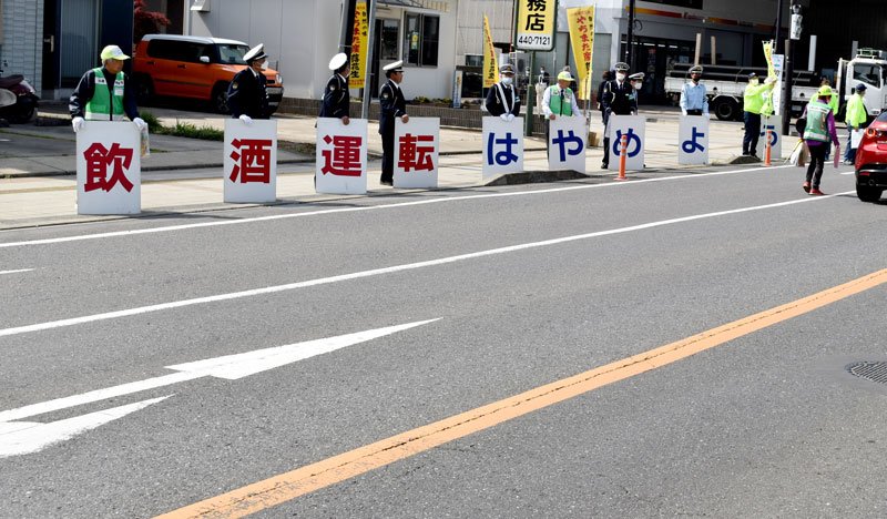 飲酒運転の撲滅へプラカードを活用してドライバーに呼びかける関係者。信号待ちの車に駆け寄り、啓発物資の配布も行った＝八街市