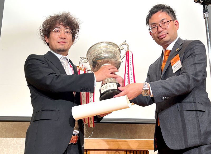最優秀賞に輝いた浅見さん（左）にＭＶＰ杯を贈る県商工会青年部連合会の荒木新五会長＝千葉市中央区のホテル