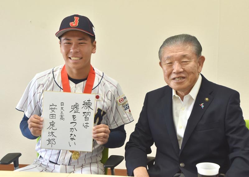自ら書いた「練習は嘘をつかない」という言葉を胸に、笑顔を見せる安田投手（左）と長谷川市長＝１８日、鴨川市