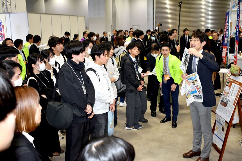 出展者（右）の説明を聞く学生ら＝２１日、都内