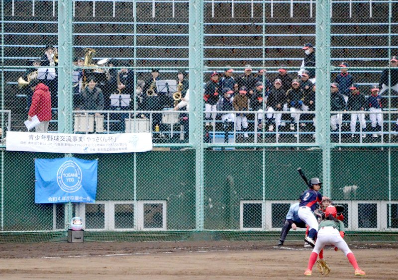 バックネット裏から高校の吹奏楽部員の応援演奏を受けて交流試合を行う少年野球チーム＝東金市