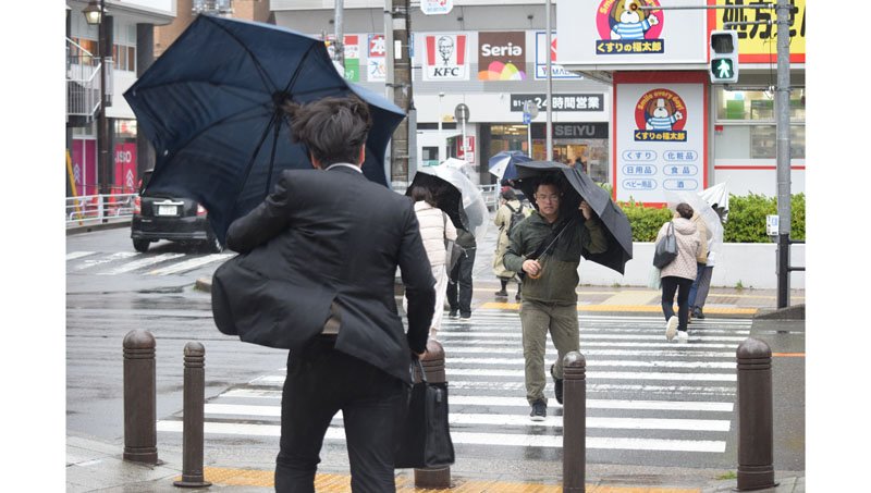 強風で傘を支えながら歩く人たち＝２９日午前１１時４５分ごろ、市川市