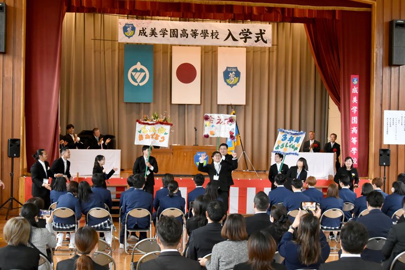 歌と踊りのパフォーマンスで新入生を歓迎する教職員＝８日、勝浦市