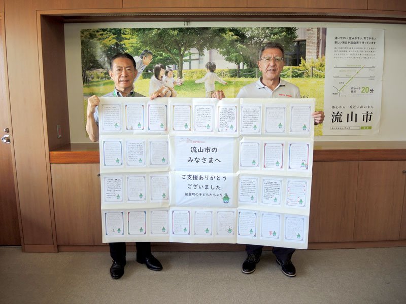 能登町の小学生から流山市に贈られた寄せ書きを手にする井崎市長（左）と大森町長＝２２日、流山市