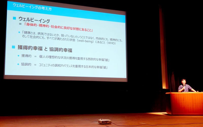 全体会の講演でウェルビーイングについて説明する南雲専務理事＝市原市民会館