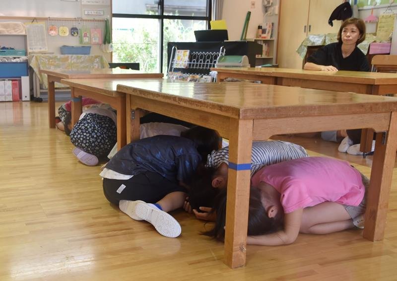 訓練で机の下に隠れ、頭を守る子どもたち＝館山市
