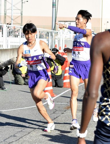 戸塚中継所でたすきをつなぐ駒大の篠原倖太朗（右）＝横浜市戸塚区
