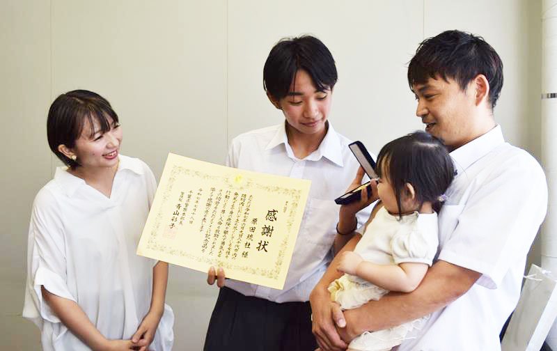 父親の辰郎さん（右）と妹の陽凪ちゃんに感謝状と記念のメダルを見せる原田さん（中央）。左は母親の友希さん＝１８日、八千代東高校