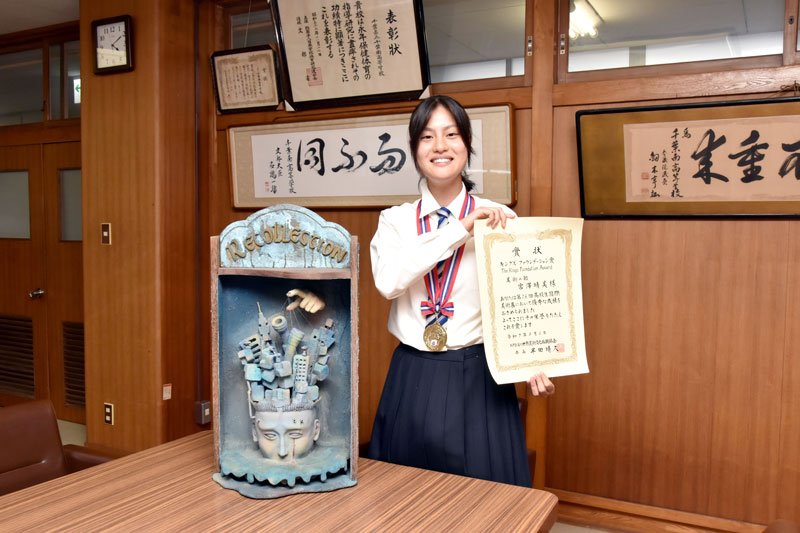 受賞作「Ｒｅｃｏｌｌｅｃｔｉｏｎ」の「コントロールされている人」の面を紹介し、賞状を手に快挙を喜ぶ宮澤さん＝千葉南高校
