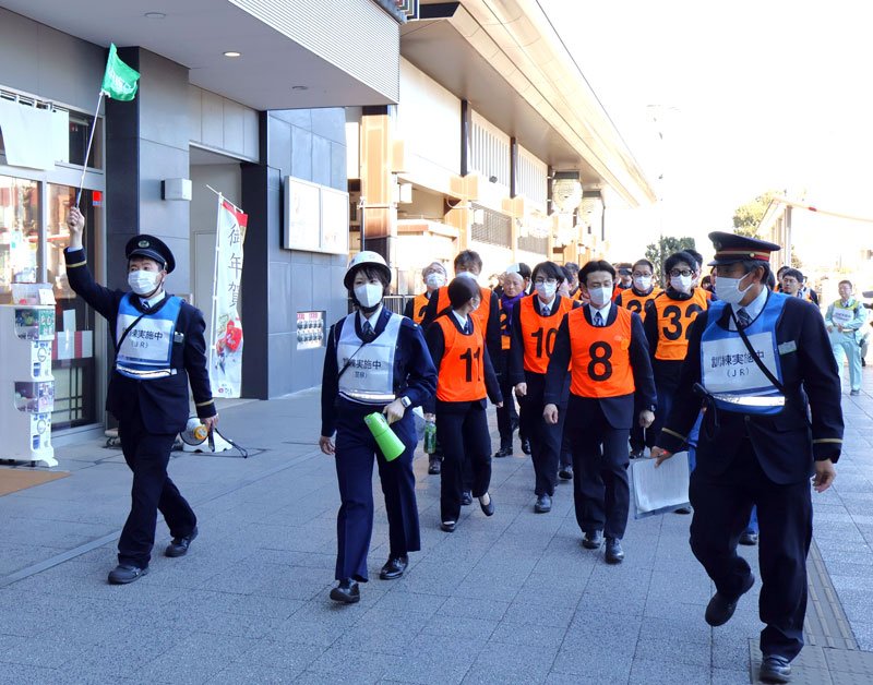 成田駅から一時滞在場所の施設まで警察官と駅員の誘導で移動する訓練参加者＝成田市