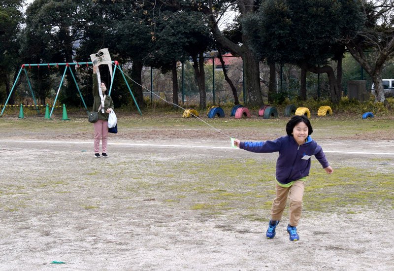 協力しながら新聞紙で作ったシンプル凧（たこ）を揚げる親子＝２０日、市原市立姉崎小