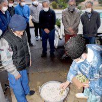作物や月別の天候などの占い項目を記した青竹を鍋に入れる松山義仁宮司（右）＝匝瑳市の中台コミュニティーセンター