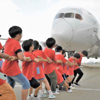 巨大な航空機を一生懸命に引っ張る子どもたち＝１７日、成田空港