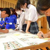 体育館や学校敷地に見立てた平面図に避難家族の情報が書かれたカードを並べて避難所開設について学ぶ栄中生＝栄町