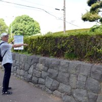 かつて高さ２００メートルの主塔が建っていた場所を示す山本会長。片側２車線の道路を挟んだ向かいの石垣の上に「船橋無線塔記念碑」が建てられている＝船橋市
