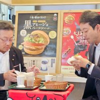 県内のモスバーガーで期間限定で発売される「黒アヒージョ　ベーコンバーガー」を試食する熊谷知事（右）とモスフードサービスの中村社長＝１日午前、千葉市若葉区