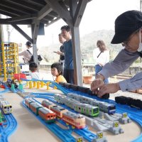 さまざまな車両の鉄道玩具を楽しむ来場者と、セッティングする関係者
